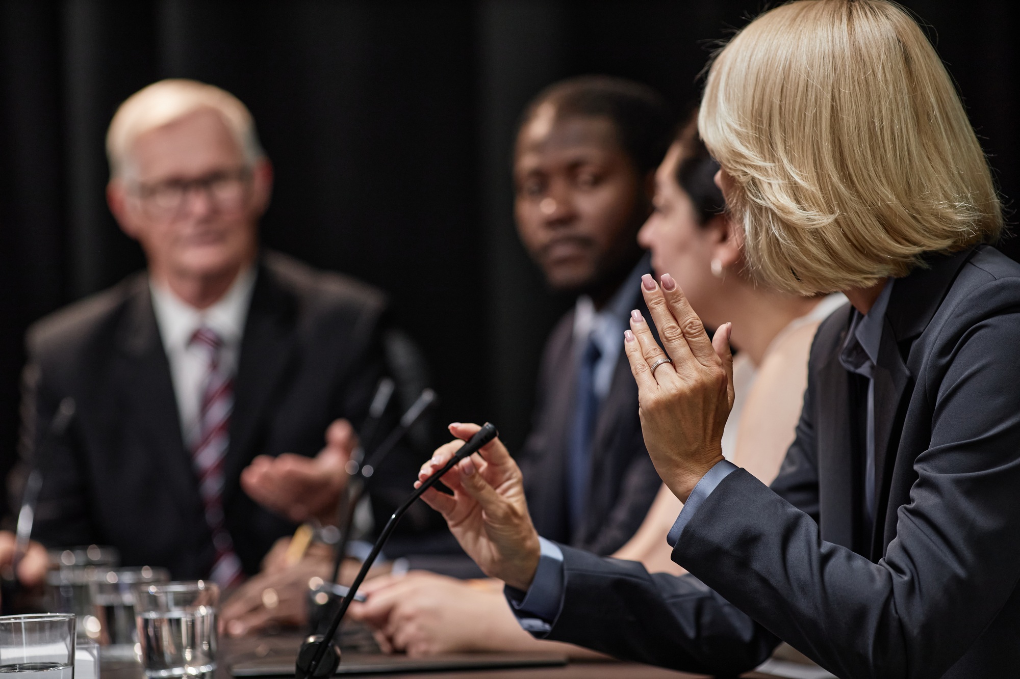 Female Politician Asking Speaker Question during Presentation while Sitting in Line with Colleagues