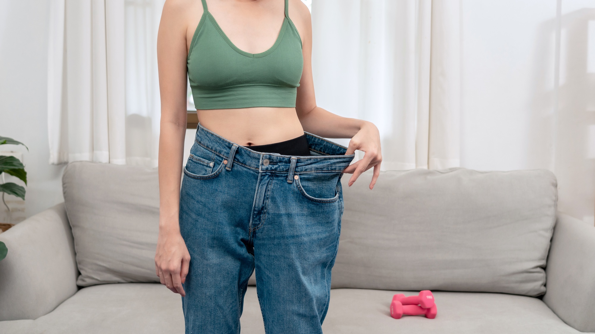 Sporty woman is smiling while wearing in loose big jean to showing successfully of weight loss